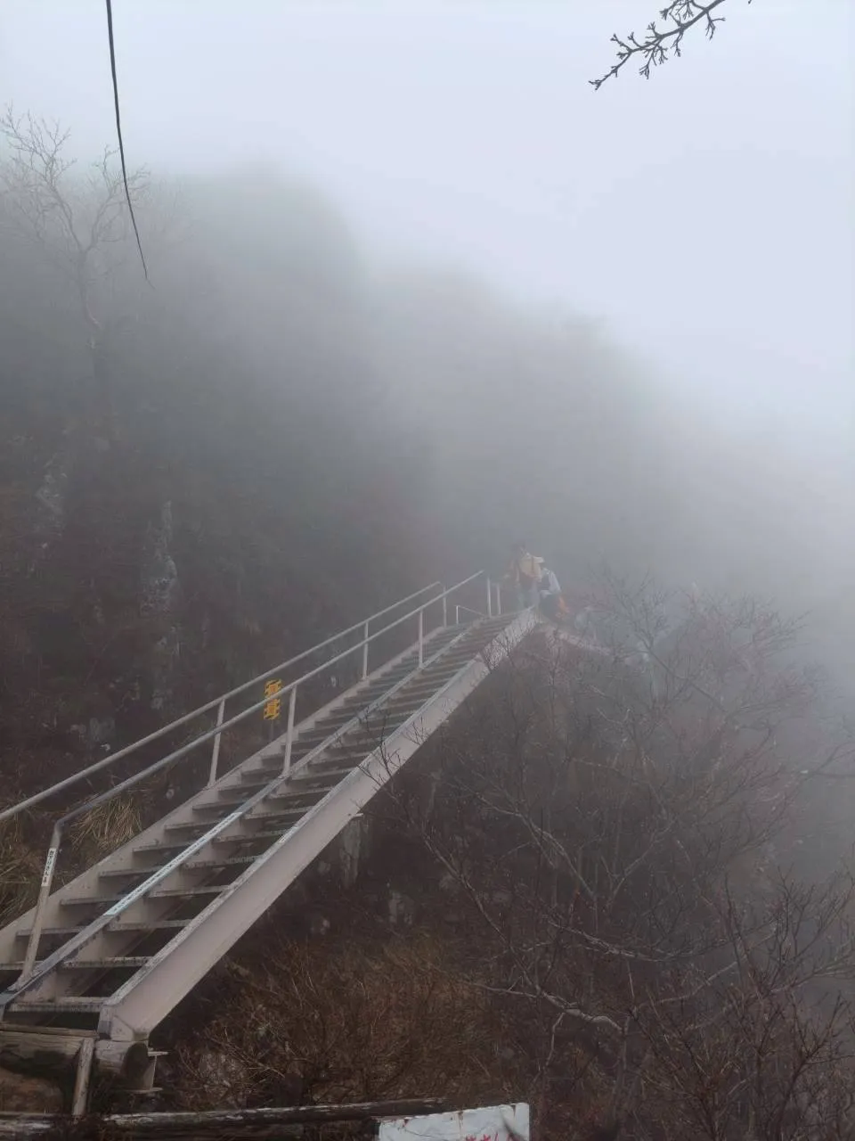 霧の中に急傾斜で伸びる鎖場の階段。上部に登山者の姿が見える。